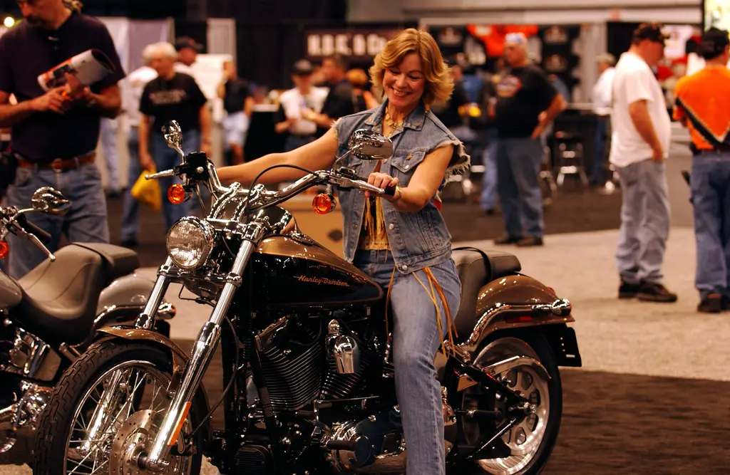 Ein Besucher sitzt auf einer schwarz-bronzenen Harley-Davidson Deuce bei einer Motorradausstellung in einer Halle.