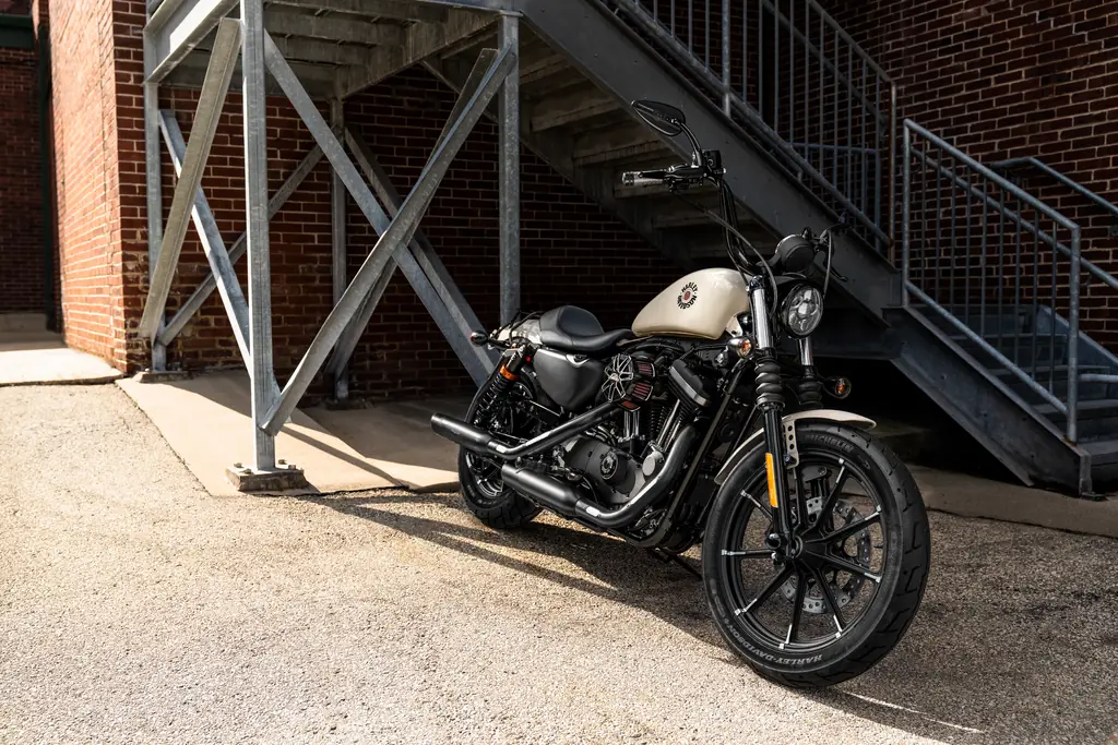 Eine Harley-Davidson Iron 883 mit cremefarbenem Tank und Original-Zubehör, unter einer eisernen Treppe geparkt