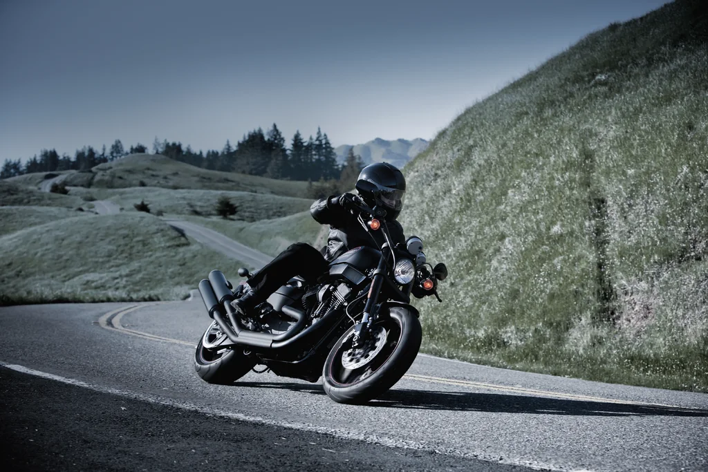 Ein Fahrer auf einer schwarzen Harley-Davidson XR1200X in Schräglage in einer Kurve auf einer Bergstraße.