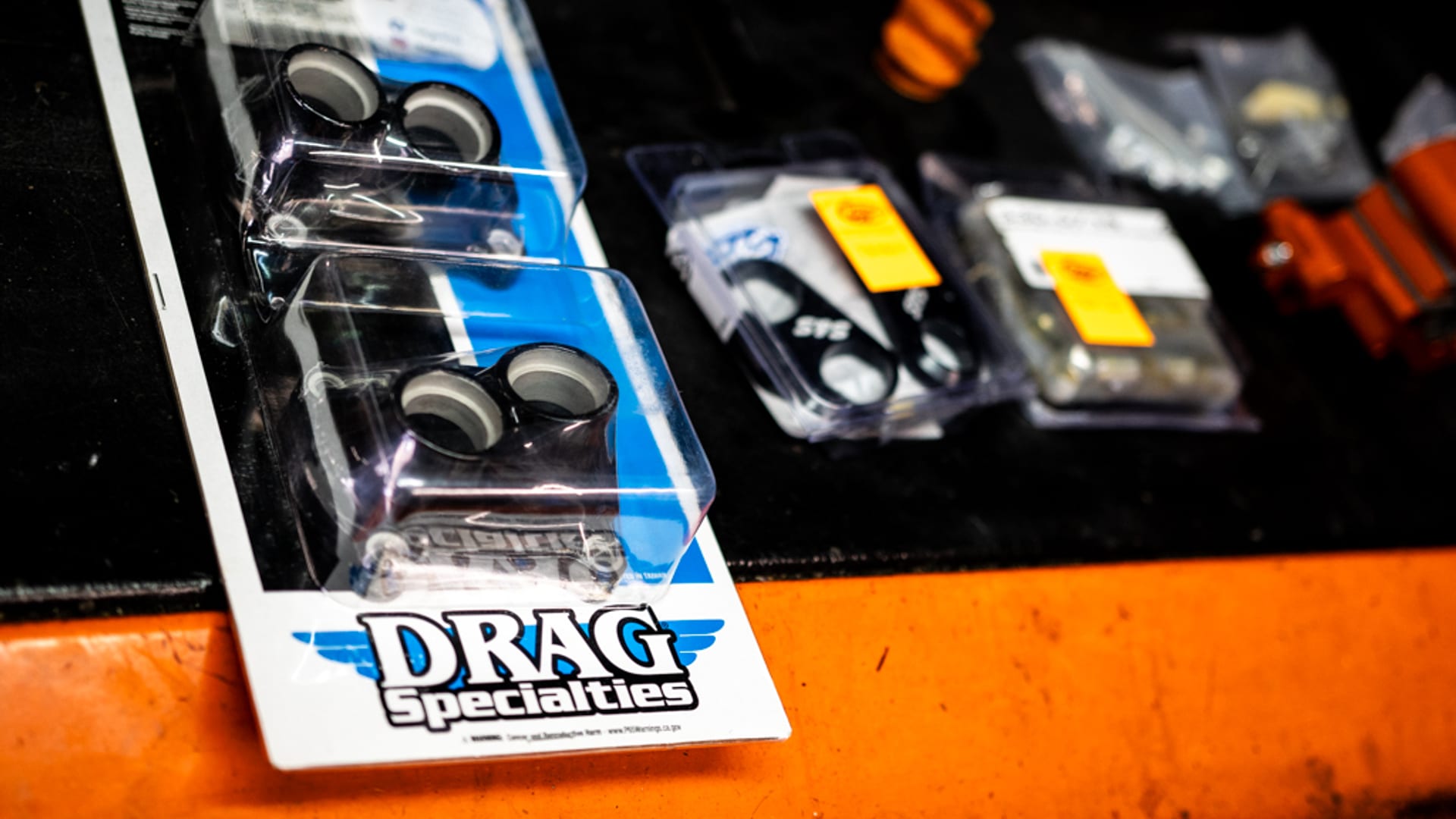 Drag Specialties Blisterverpackung auf dunkler Werkstattbank — die typische blau-weiße Verpackung